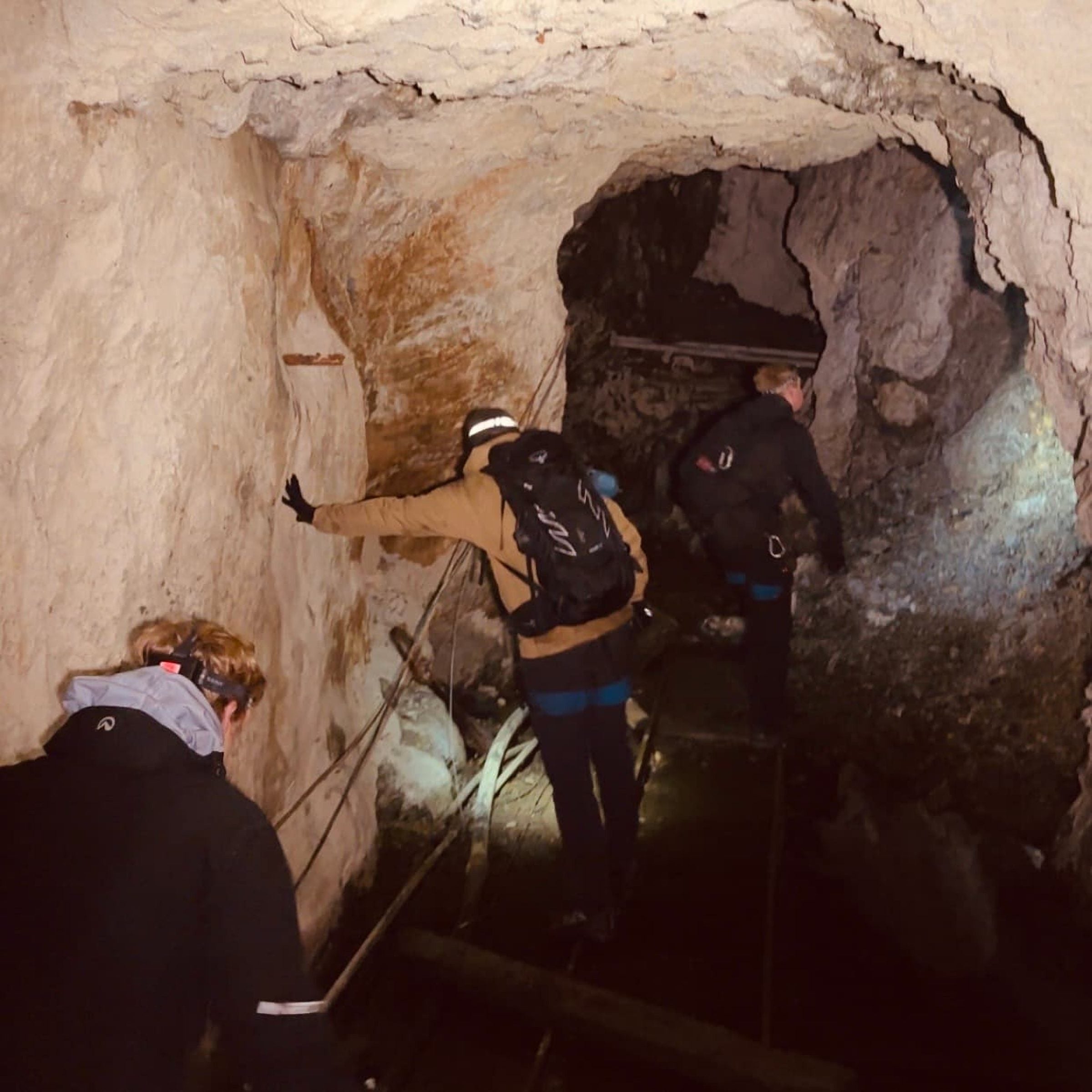 To personer med hodelykt og sekk i en grotte